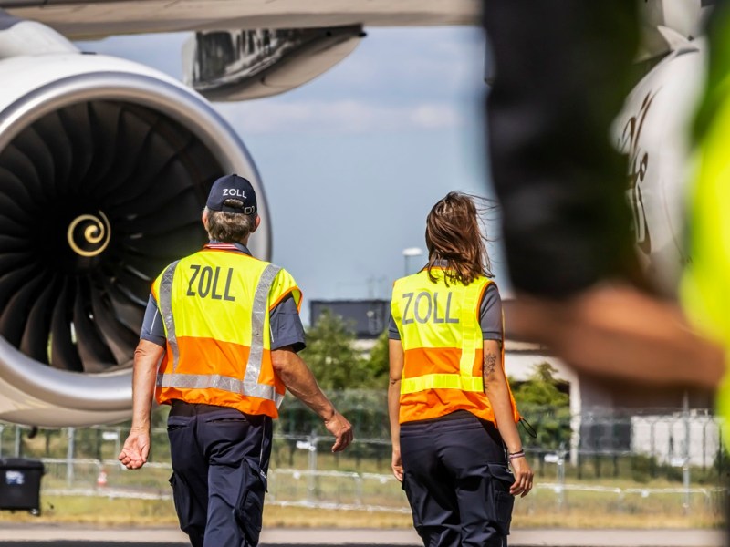 Zwei Zoll-Mitarbeiter stehen auf dem Rollfeld des Flughafens BER.